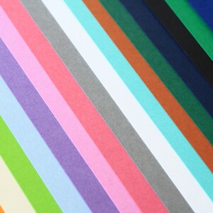 May include: A collection of colorful paper strips arranged in a diagonal pattern. The colors include orange, yellow, green, light blue, purple, pink, red, gray, white, turquoise, brown, dark green, navy blue, black, and dark blue.