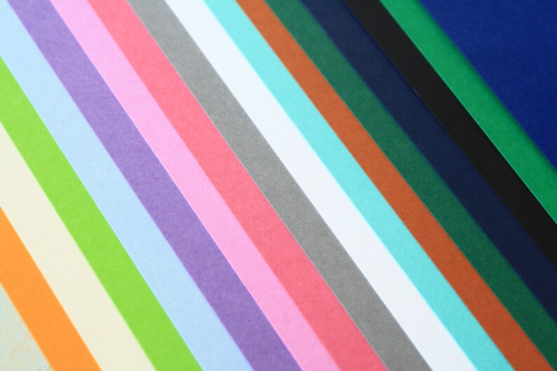 May include: A collection of colorful paper strips arranged in a diagonal pattern. The colors include orange, yellow, green, light blue, purple, pink, red, gray, white, turquoise, brown, dark green, navy blue, black, and dark blue.