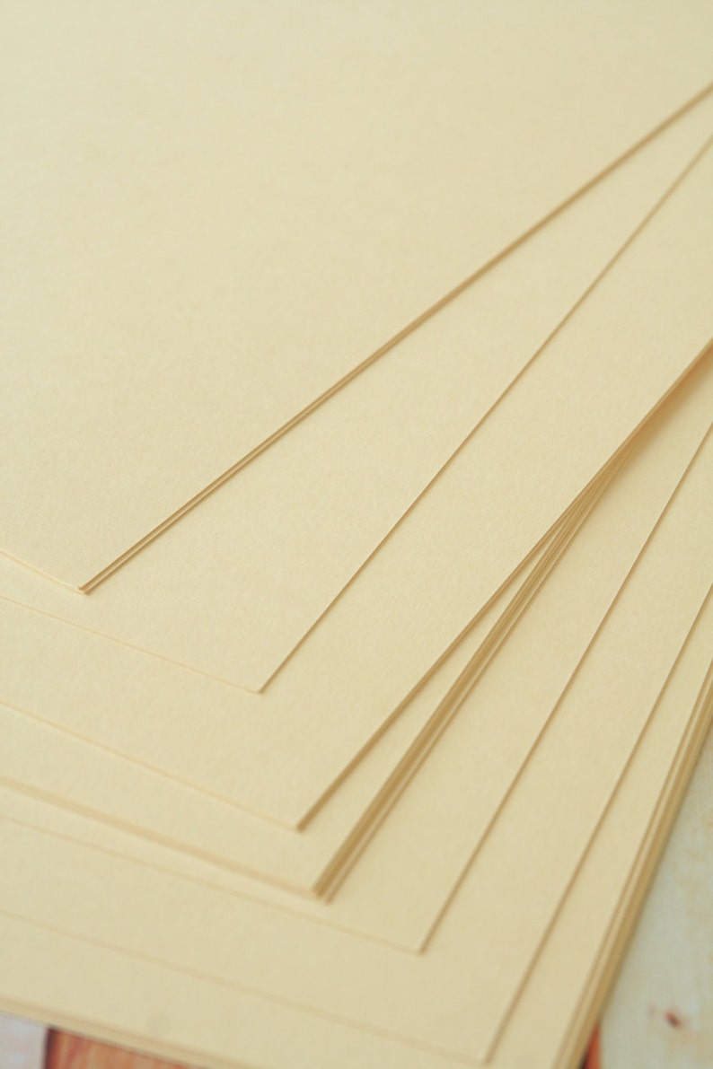 May include: A stack of cream-colored paper sheets, arranged in a fan shape, with the top sheet folded over the others.