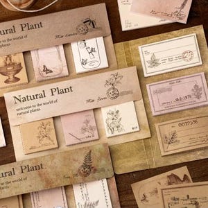 May include: A white ceramic mug with a black handle and the text "But First, Coffee" in a handwritten style. The mug is on a white surface. The mug is approximately 10 cm tall.