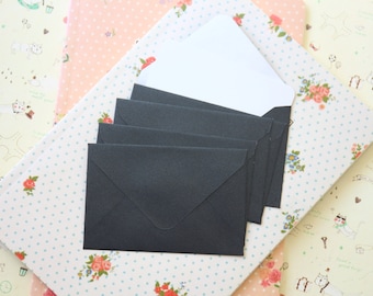 May include: A stack of five black envelopes on a patterned background. The envelopes are folded and ready to be used for sending letters or cards.