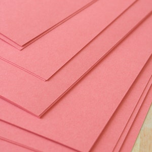 May include: Stack of pink construction paper. The paper is smooth and has a slight sheen.