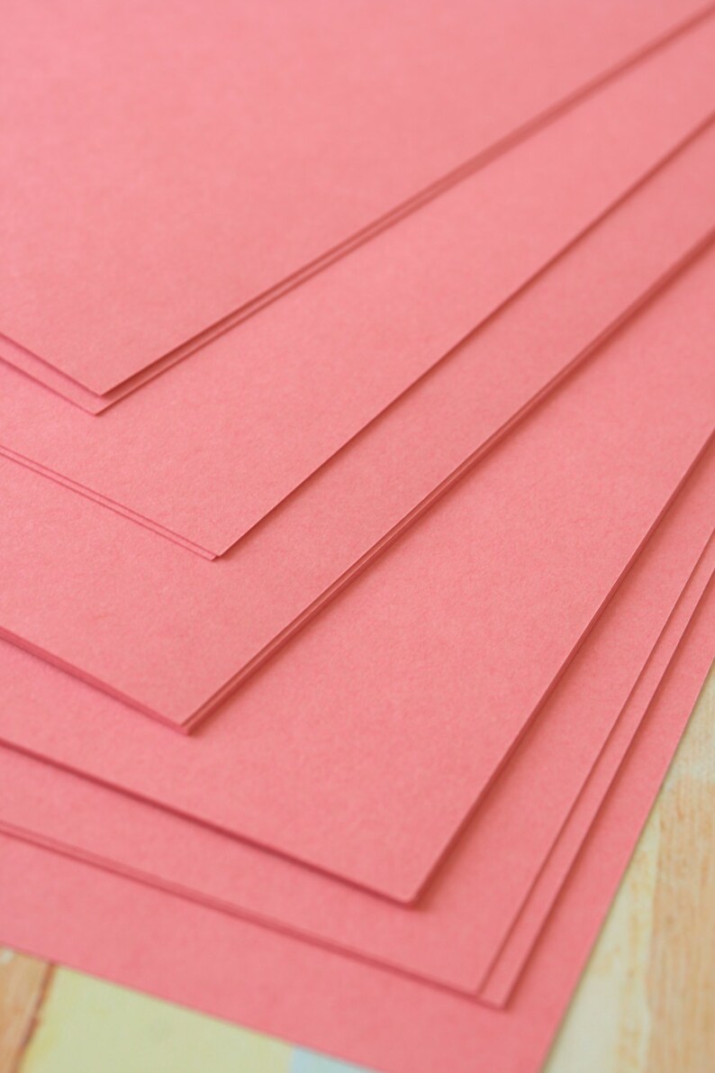 May include: Stack of pink construction paper. The paper is smooth and has a slight sheen.