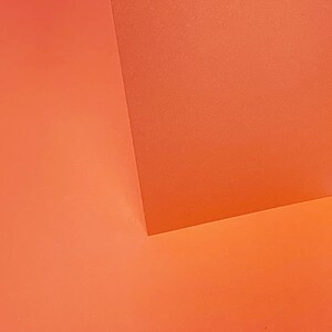 May include: Two pieces of orange colored paper meet at a corner, creating a geometric pattern.