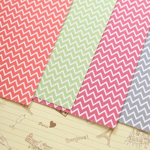 Pode incluir: Quatro folhas de papel estampado com um padr&atilde;o chevron. O papel &eacute; em tons de rosa, verde e cinza.