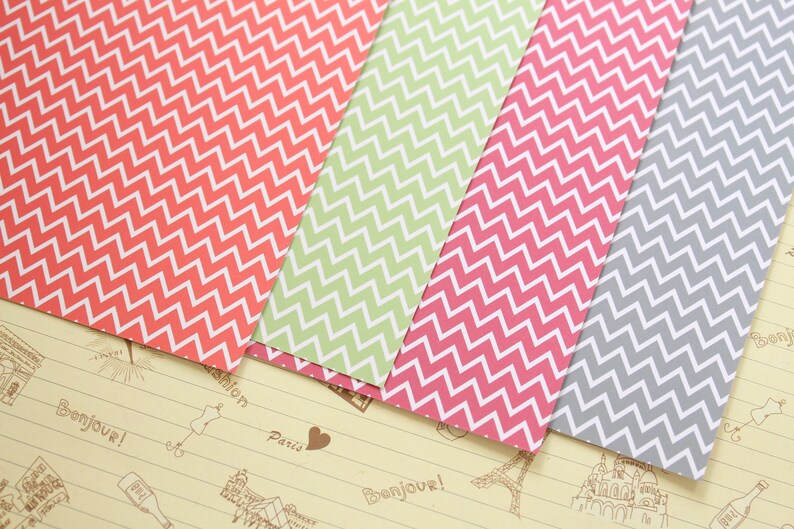 Pode incluir: Quatro folhas de papel estampado com um padr&atilde;o chevron. O papel &eacute; em tons de rosa, verde e cinza.