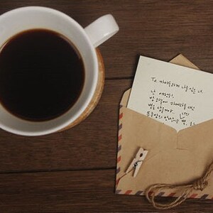 May include: A brown envelope with a handwritten note inside. The note says "To my love, I love you so much. I miss you. I wish you were here. We can overcome..." The envelope is tied with twine and has a small wooden peg attached.