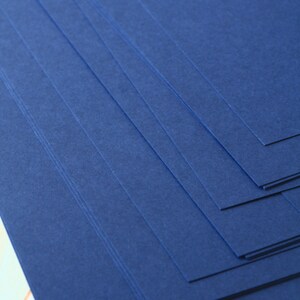 May include: Stack of dark blue cardstock paper. The paper has a textured surface.