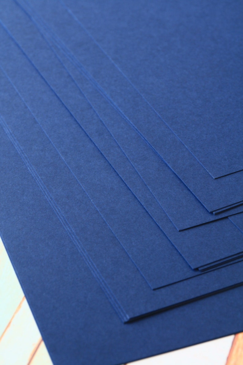 May include: Stack of dark blue cardstock paper. The paper has a textured surface.