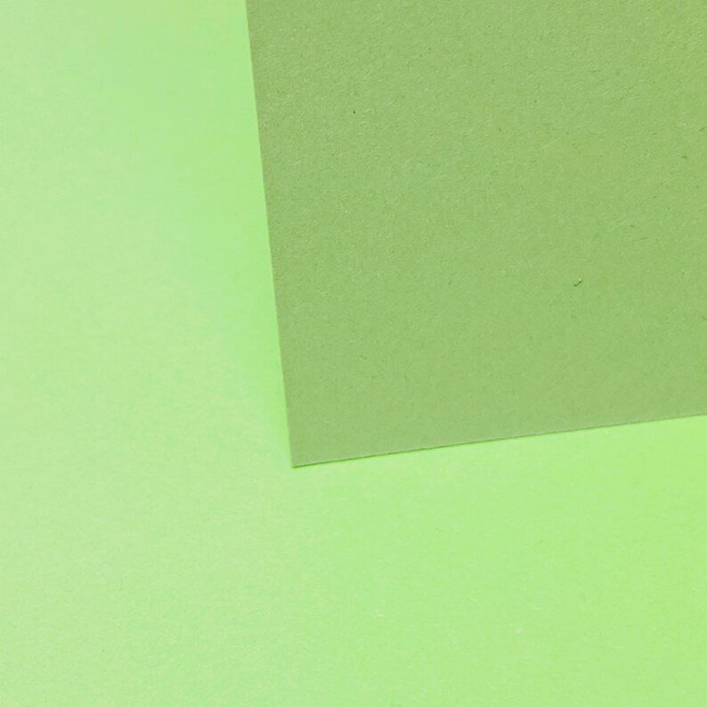 May include: Two pieces of green paper, one on top of the other, creating a diagonal line. The top piece of paper is a slightly darker shade of green.