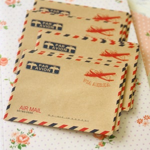 May include: A stack of brown airmail envelopes with red and blue stripes. The envelopes feature a vintage airplane design and the text "Par Avion" and "Via Aerea".