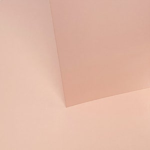 May include: A close-up of two pieces of pale pink paper, one on top of the other, creating a subtle shadow effect.