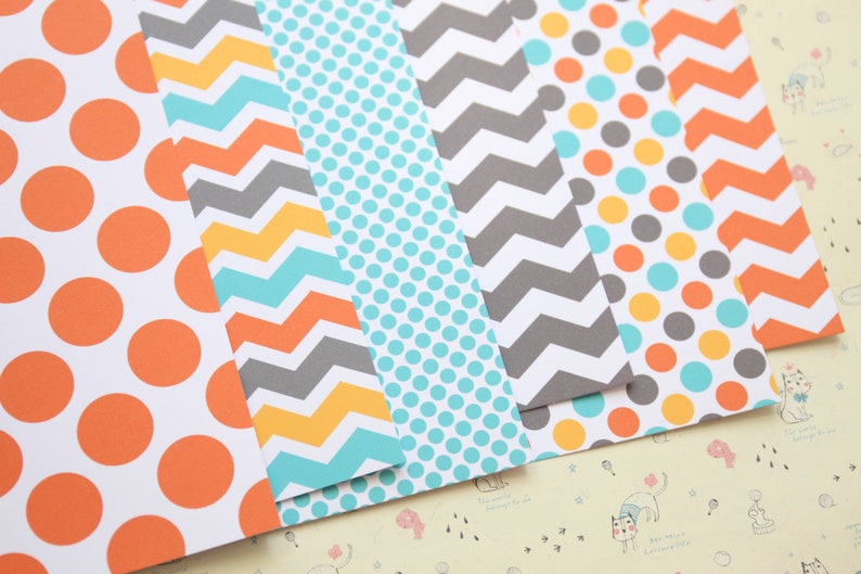 May include: Six sheets of patterned paper with different designs. The designs include orange and white polka dots, yellow and gray chevron, turquoise and white polka dots, gray and white chevron, turquoise and yellow polka dots, and orange and gray chevron.