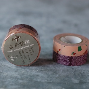 May include: Two rolls of washi tape, one with a pink and green floral pattern and the other with a purple lace pattern. The label on the floral roll reads "夜長堂印 Washi paper adhesive tape".