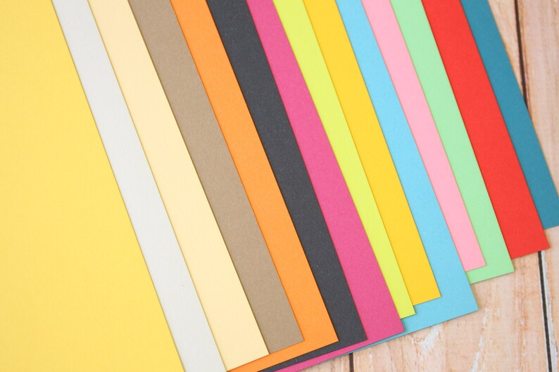 May include: A collection of colorful paper sheets arranged in a diagonal pattern. The colors include yellow, white, light yellow, brown, orange, black, pink, green, light blue, blue, and red.