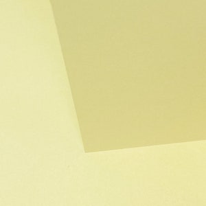 May include: Two pieces of paper, one a pale yellow and the other a slightly darker yellow, are placed next to each other. The darker yellow paper is on top of the lighter yellow paper, and the corner of the darker yellow paper is folded over the lighter yellow paper.