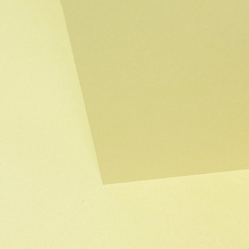 May include: Two pieces of paper, one a pale yellow and the other a slightly darker yellow, are placed next to each other. The darker yellow paper is on top of the lighter yellow paper, and the corner of the darker yellow paper is folded over the lighter yellow paper.