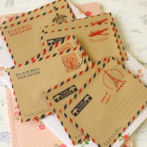 May include: A set of six brown paper envelopes with red and blue stripes. The envelopes have a vintage look and are decorated with stamps and text that says "By Air Mail Par Avion".
