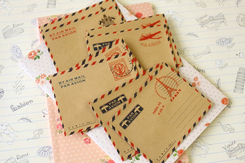 May include: A set of six brown paper envelopes with red and blue stripes. The envelopes have a vintage look and are decorated with stamps and text that says "By Air Mail Par Avion".
