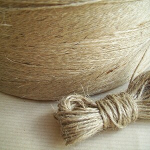 May include: A roll of natural twine, made from jute fiber, is shown with a loose end of the twine. The twine is a light brown color and has a rough texture.