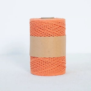 May include: A spool of orange cotton cord wrapped in brown paper. The cord is made from natural fibres and is ideal for crafting projects.