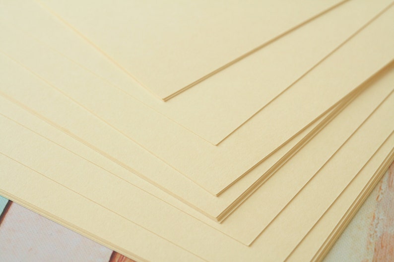 May include: A stack of cream-colored paper sheets, arranged in a diagonal pattern.