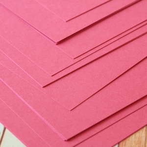 May include: A stack of red construction paper sheets, arranged in a diagonal pattern. The paper has a slightly textured surface.