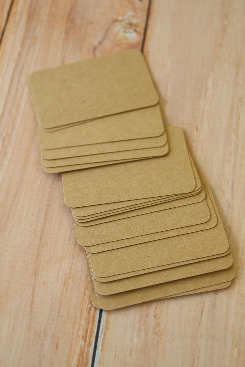 May include: A stack of rectangular, light brown kraft paper cards with rounded corners. The cards are arranged in a slightly fanned, overlapping pile, displaying a smooth, matte texture and a consistent, neutral tan color throughout the set.