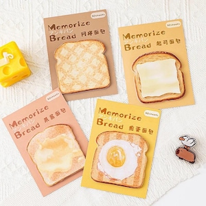 May include: Four rectangular packages of sticky notes, each featuring a slice of bread with different toppings: a waffle-patterned slice, a cheese slice, a jam-covered slice, and a fried egg slice. Each package is labeled Memorize Bread.