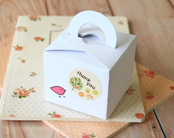 May include: White gift box with a handle, decorated with a sticker that says "thank you" and features a small bird and floral design.