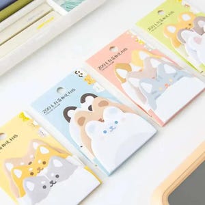 May include: Three rectangular packs of animal-shaped sticky notes featuring cartoon bear and cat designs. Each pack displays the text ZOO系列动物便利贴 and contains multiple layered adhesive paper sheets in pastel colors including blue, pink, and yellow.