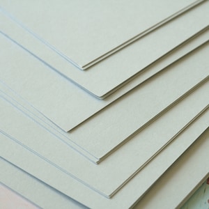 Może przedstawiać: Stos jasnoszarego papieru kartonowego.
