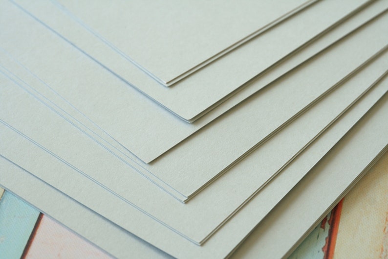 Może przedstawiać: Stos jasnoszarego papieru kartonowego.