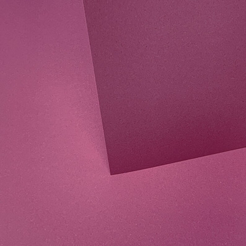 May include: Two pieces of textured paper, one a darker shade of pink and the other a lighter shade of pink, are joined at a corner to form a right angle.