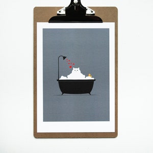 May include: A print of a white cat in a black bathtub with bubbles, a yellow rubber duck, and red hearts showering from a black shower head. The print is on a white-bordered gray background, clipped to a brown clipboard.
