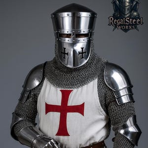 May include: A full suit of medieval armor, including a helmet, chainmail, and plate armor. The white tunic features a large red cross. A sword is held in the right hand. The logo for Regal Steel Works is in the upper right corner.