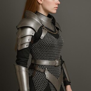 May include: A silver-colored medieval armor set, including shoulder pauldrons, a gorget, and arm guards. The armor is worn over a chainmail shirt and a leather belt. The overall design is detailed and realistic, suitable for cosplay or historical reenactment.
