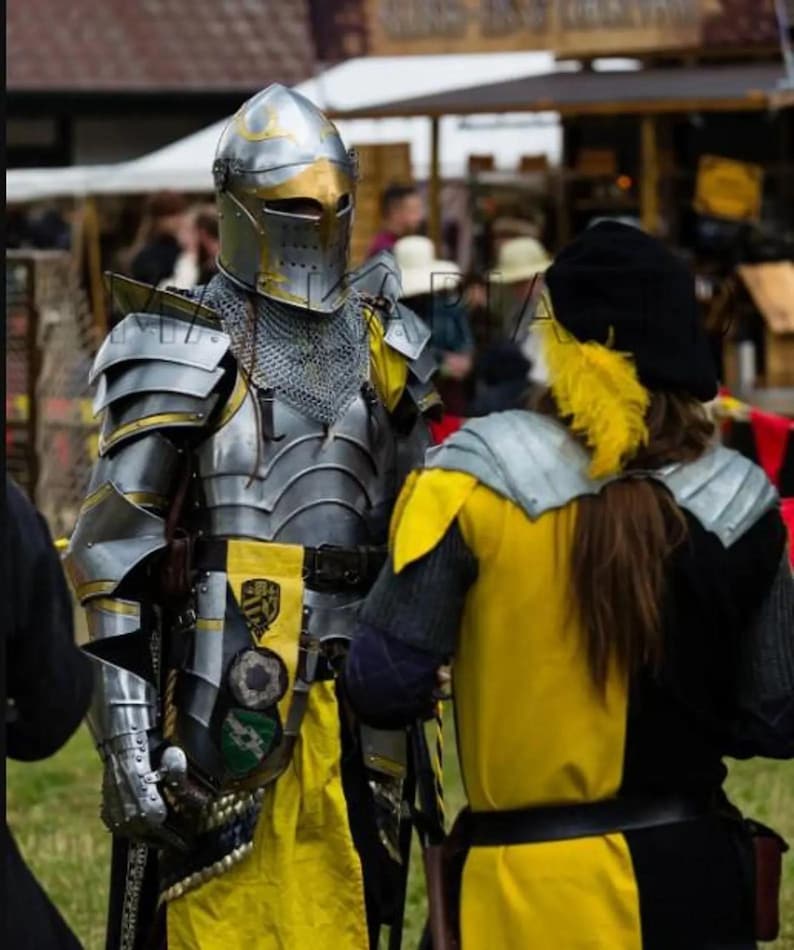 May include: A person in medieval armor stands next to another person in a yellow and black tunic. The armor is silver and gold, with a helmet and chainmail. The tunic has a yellow and black color scheme.