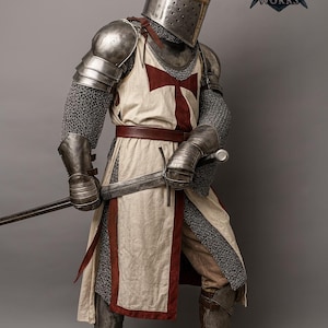 May include: A medieval knight in full armor, including a helmet, chainmail, and metal shoulder guards. The knight wears a white tunic with a red cross and holds a sword. The image includes the "Regal Steel Works" logo.