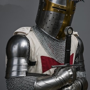 May include: A knight's full suit of armor, including a helmet with gold accents, chainmail, and metal shoulder and arm guards. The knight is holding a sword. The white tunic has a red cross. The Regal Steel Works logo is visible.
