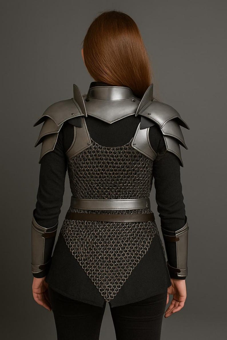 May include: A silver-colored fantasy armor set, including shoulder pauldrons, a neck guard, and chainmail. The armor is worn over a black long-sleeved top and is secured with a belt. The set also includes arm guards.