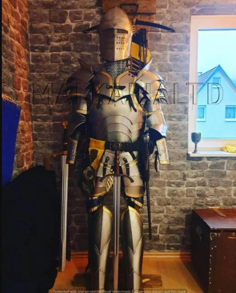 May include: A full suit of medieval armor, including a helmet, chest plate, and leg guards, displayed on a stand. The armor is primarily silver with gold and black accents. Two swords are positioned nearby, suggesting a historical or fantasy theme.