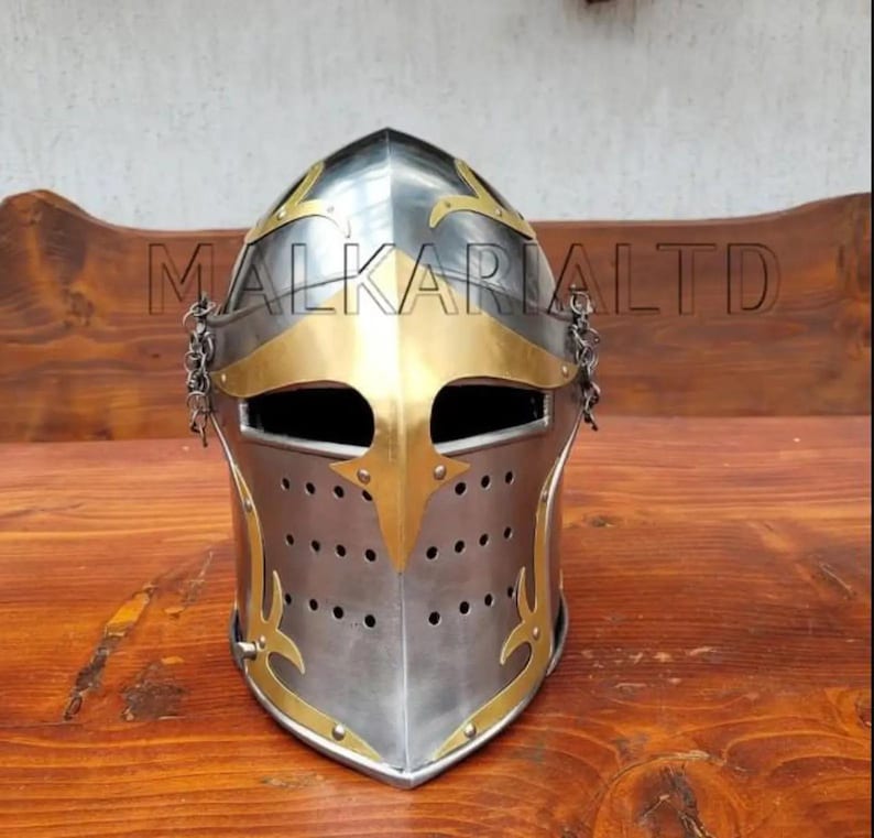 May include: A silver and gold medieval helmet with a riveted construction. The helmet features decorative gold accents, a visor, and a chainmail neck guard. The text "MALKARIALTD" is printed across the top of the helmet.