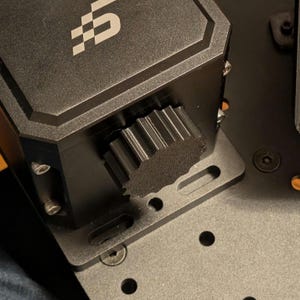 Könnte beinhalten: Eine schwarze Metallbox mit einem Zahnradknopf an der Seite. Die Box ist auf einer schwarzen Metallplatte mit mehreren Löchern montiert.