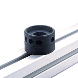 May include: A black cylindrical component featuring evenly spaced circular perforations. It rests on a silver metal rail, set against a white backdrop.