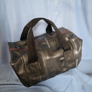 May include: A black duffel bag made from recycled bicycle inner tubes. The bag has a red zipper and black straps. The bag has the word "future" printed on the side.