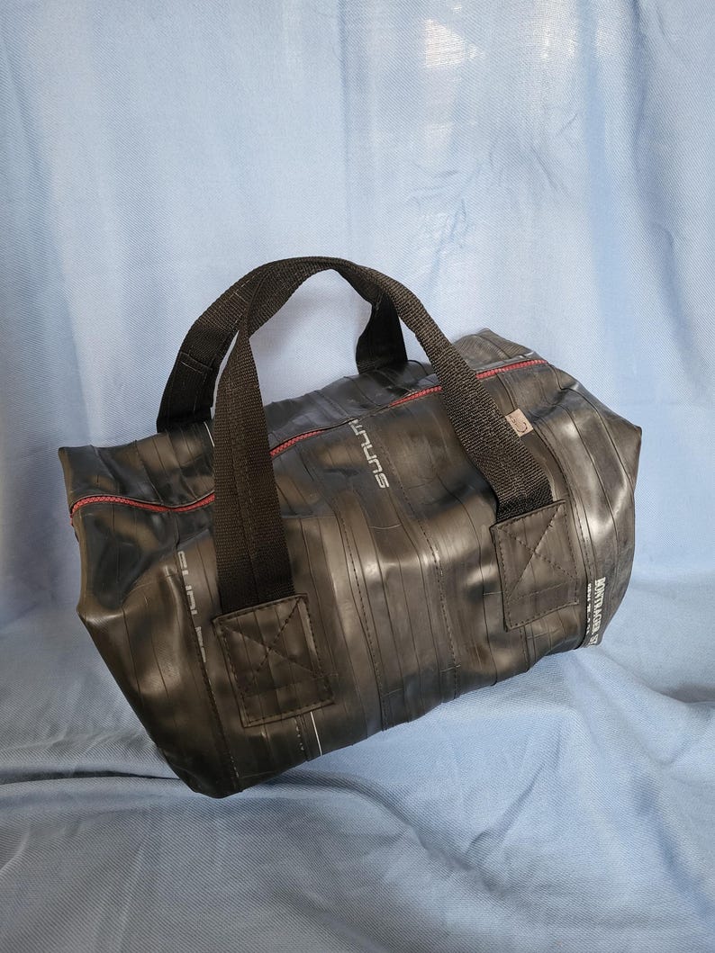 May include: A black duffel bag made from recycled bicycle inner tubes. The bag has a red zipper and black straps. The bag has the word "future" printed on the side.
