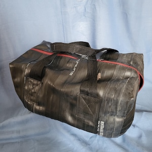 May include: Black duffel bag made from recycled tire inner tubes with red zipper and black straps. The bag has the text "Bontrager TLR" printed on the side.