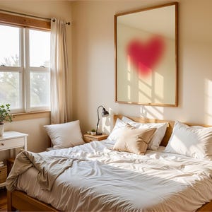 May include: A bedroom with a large window, white curtains, a wooden bed frame, white bedding, and a framed mirror with a red heart shape in the center.