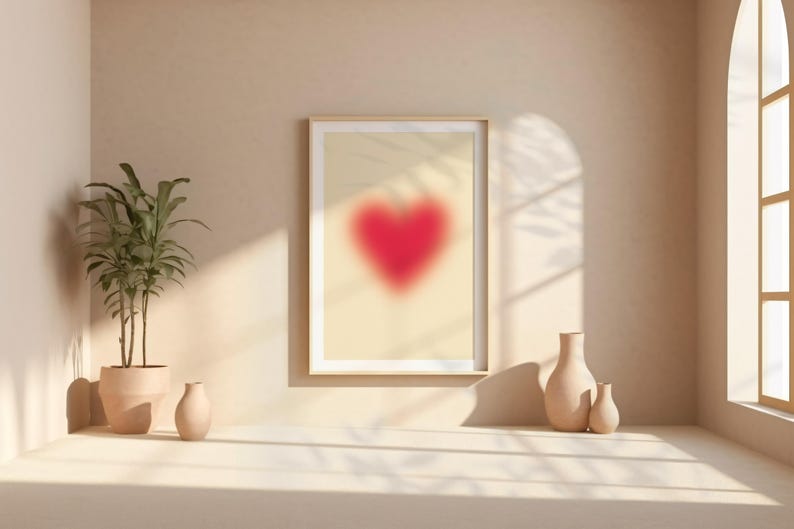 May include: A framed print of a blurred red heart on a beige background, with a potted plant and two ceramic vases on a white surface.